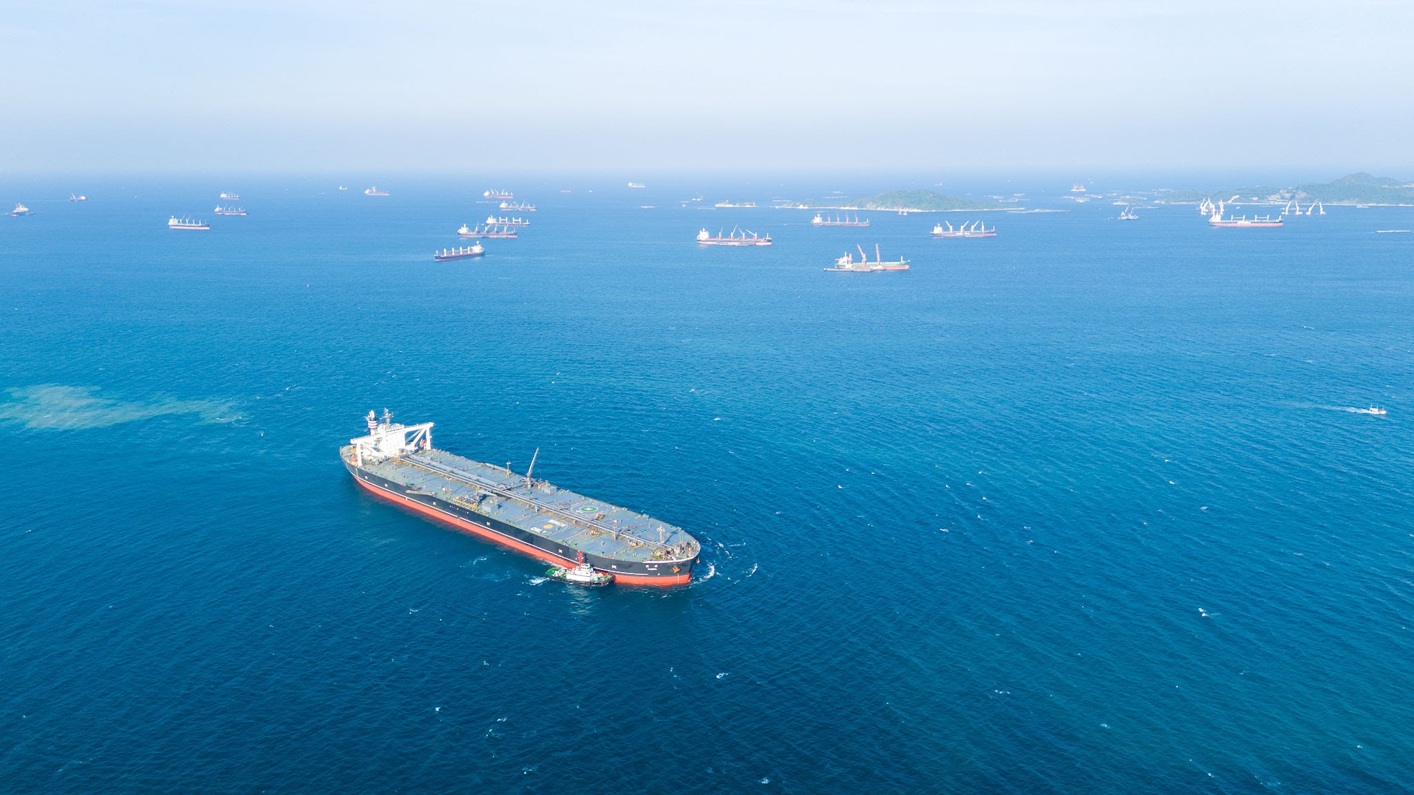 Massive crude oil tanker ship assisted by tugboats while sailing across the deep blue ocean. Global maritime logistics, fossil fuel energy, and heavy industrial transport business concept.