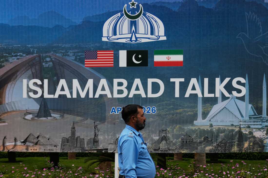A police officer walks past a billboard regarding the United States and Iran negotiations, outside a media facilitation center in Islamabad, Pakistan, Saturday, April 11, 2026. (AP Photo/Anjum Naveed)