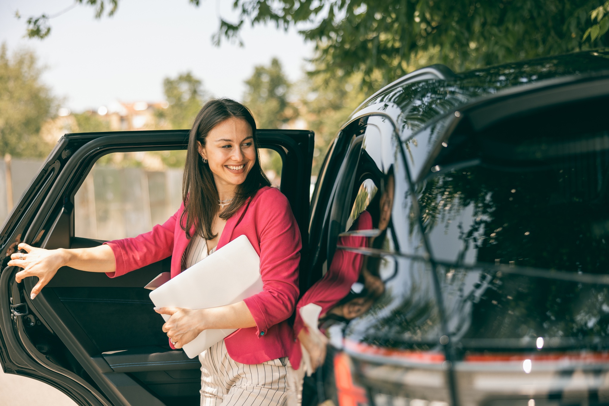 Young confident woman getting out of the car with her laptop and going to work. 